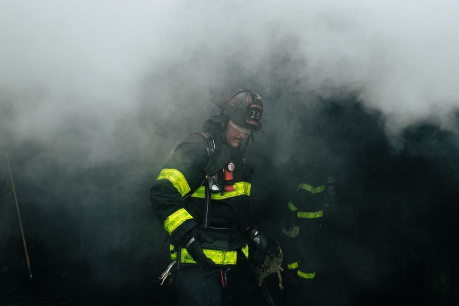 A firefighter walks out of heavy smoke in turnout gear