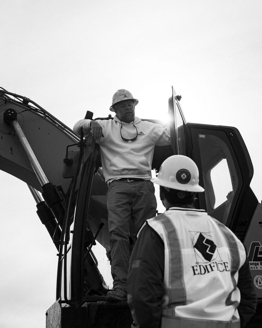 Two operators in hard hats talk on an excavator