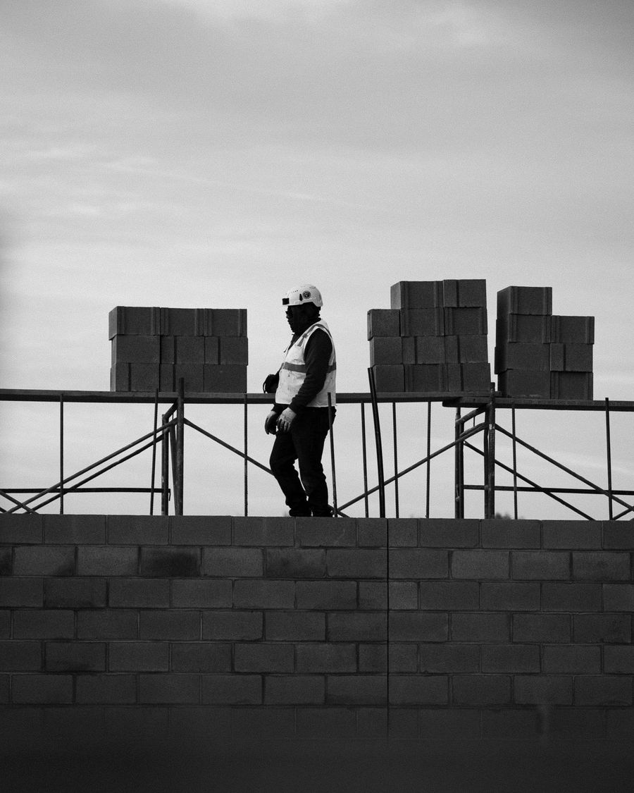 A mason stands on a block wall against the sky