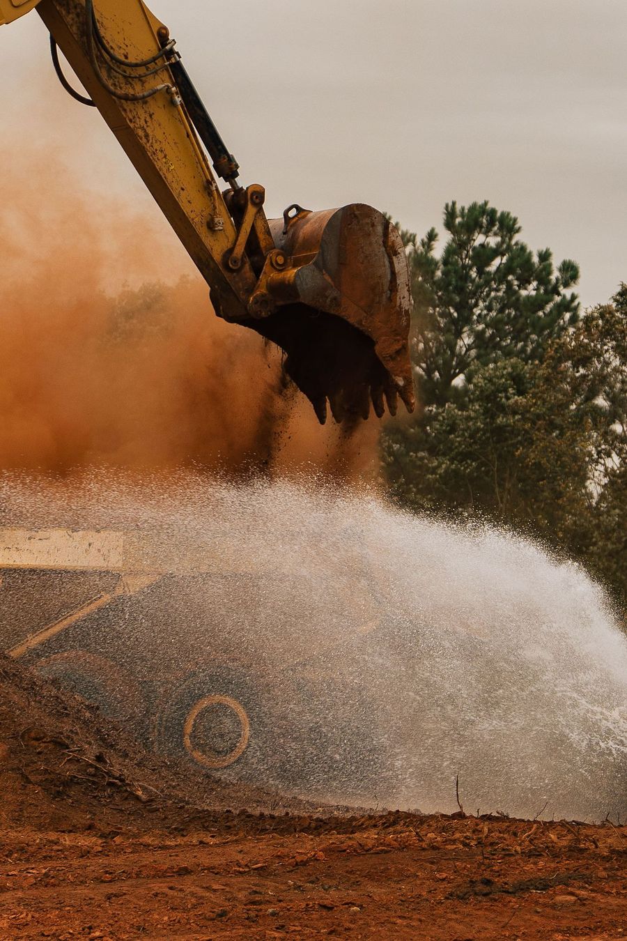 Water sprays across red clay beside an excavator