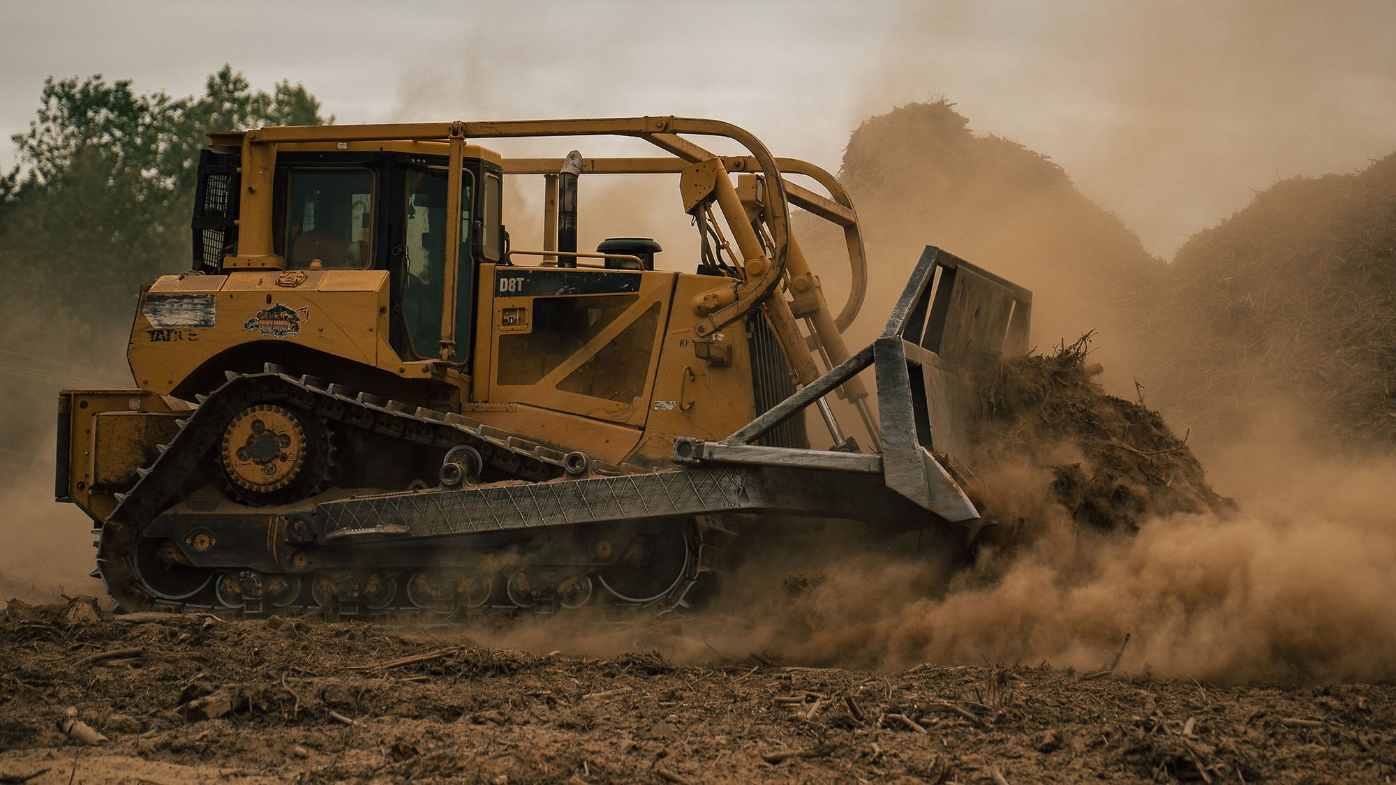A Cat D8T dozer pushes a pile of debris through a cloud of dust on a land clearing job