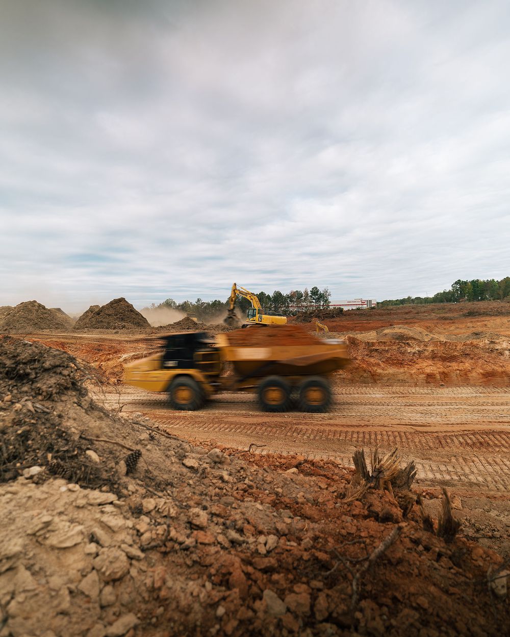 An articulated dump truck blurs past a red clay cut on an active grading site